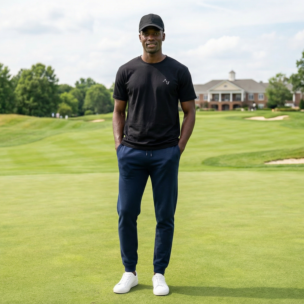 Man standing on a golf course wearing a black cap, black shirt, and blue pants.