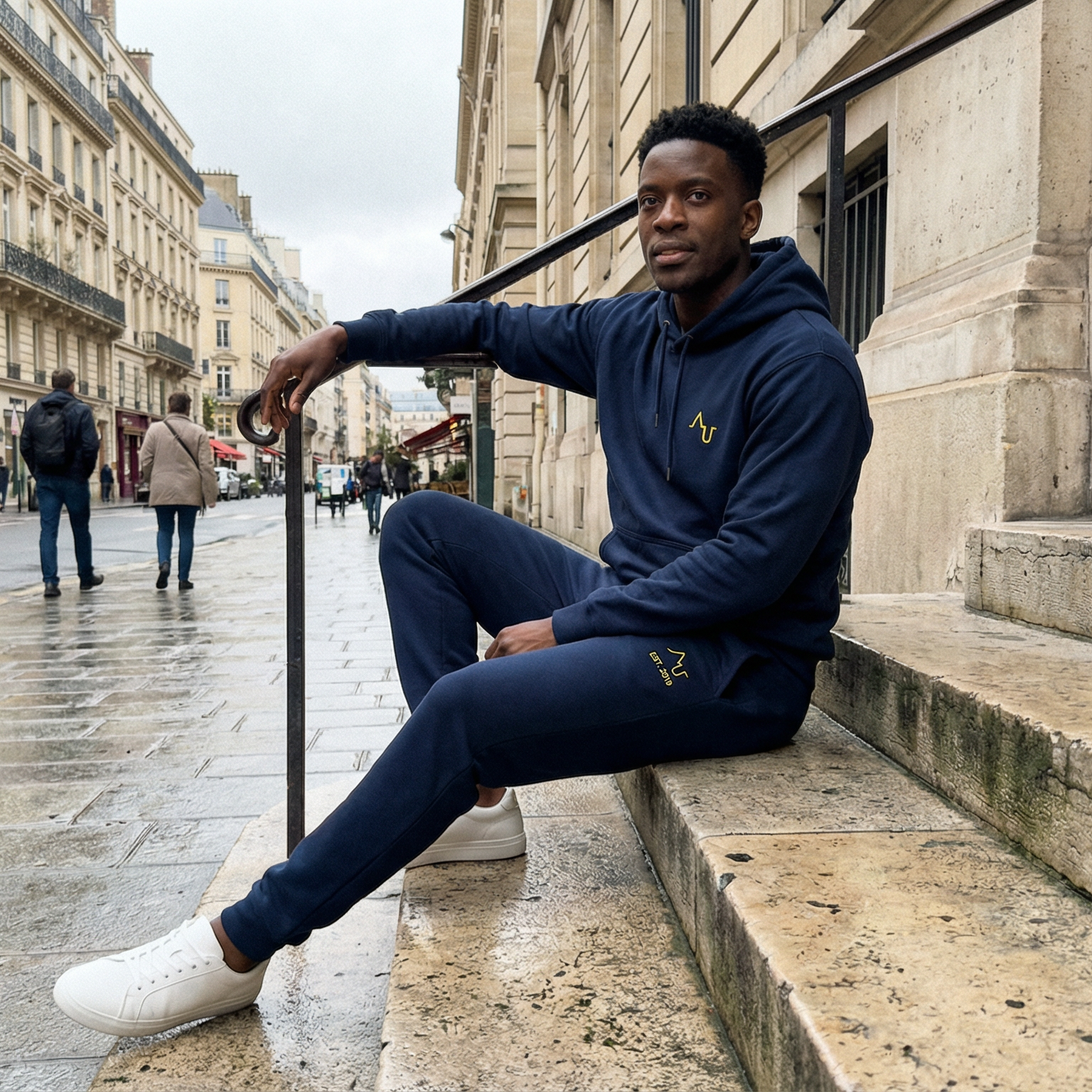 Man sitting on steps in an urban setting wearing a navy tracksuit.