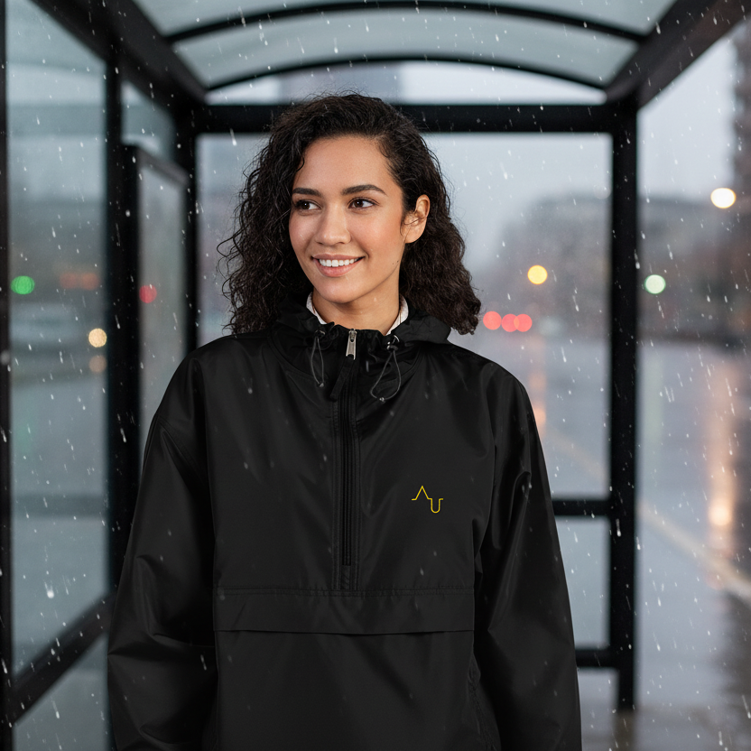 Woman wearing a black raincoat standing in a bus shelter on a rainy day.