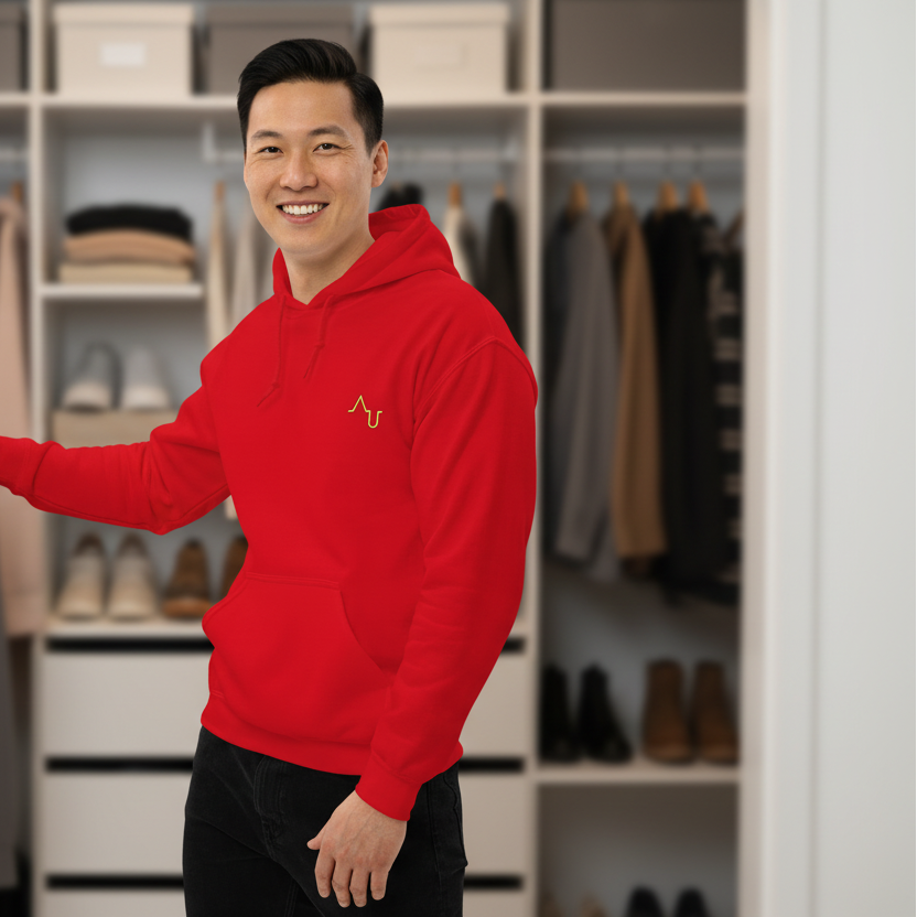 Man wearing a red hoodie with a logo in a closet filled with clothes and shoes.